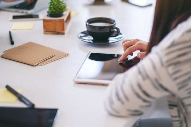 Una mujer que usa y señala con el dedo a un tablet pc con una taza de café sobre la mesa