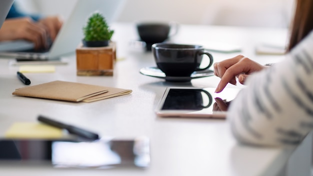 Una mujer que usa y señala con el dedo a un tablet pc con una taza de café sobre la mesa