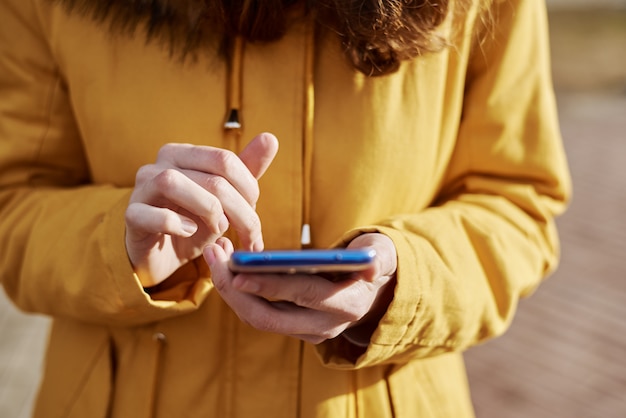 Mujer que usa smartphone en la ciudad al aire libre, de cerca. Manos femeninas escribiendo mensajes en el teléfono móvil