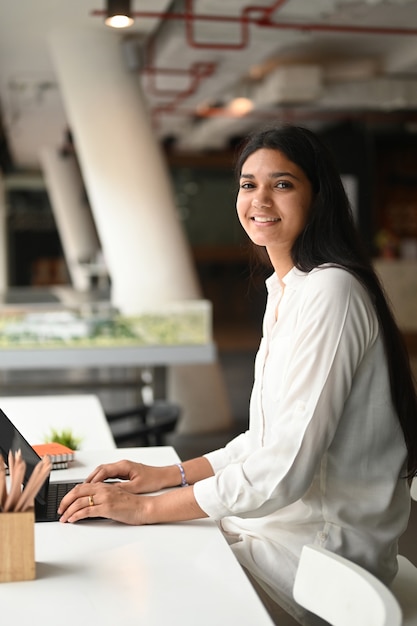 Mujer que usa una tableta de computadora mientras está sentado en el escritorio de trabajo blanco