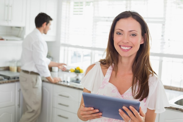 Mujer que usa la tableta digital con el hombre en el fondo en la cocina