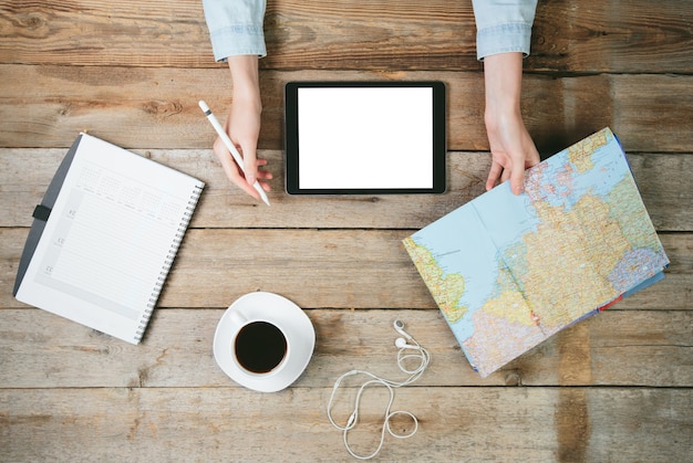 Mujer que usa una tableta en el escritorio con un mapa del mundo y una taza de café junto a ella. Ella esta sosteniendo un lapiz