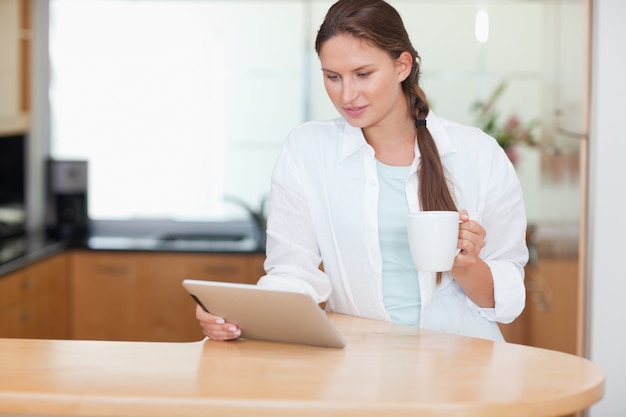 Mujer que usa una tableta mientras que bebe té