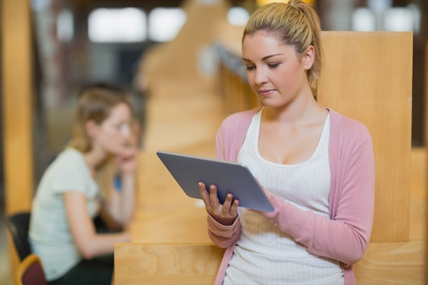 Mujer que usa la tableta que se coloca en biblioteca de la universidad