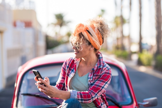 Mujer que usa el teléfono al aire libre en viajes de la vida real y coche de vacaciones de vacaciones de verano para mujer conductora