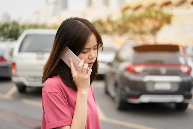 Mujer que usa el teléfono inteligente para la aplicación en el fondo de la falta de definición del coche.