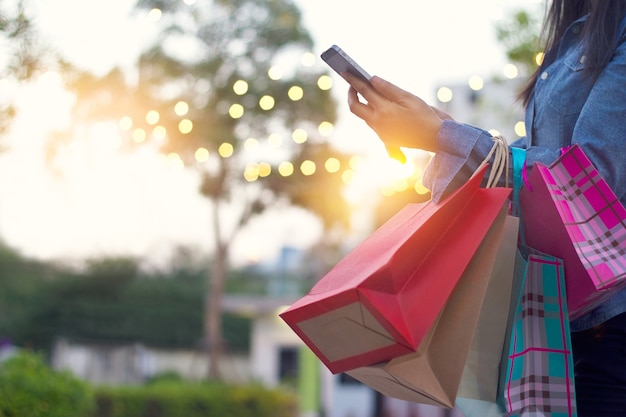 Foto mujer que usa el teléfono inteligente con el bolso de compras en manos