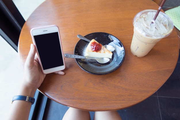 Mujer que usa el teléfono inteligente en la cafetería con café y pastel