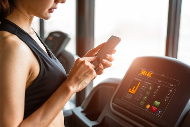 Mujer que usa un teléfono inteligente cuando entrena o entrenamiento de fuerza en el gimnasio