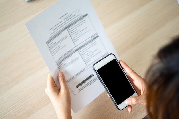 Mujer que usa un teléfono inteligente para escanear un código de barras para pagar varios gastos con tarjeta de crédito