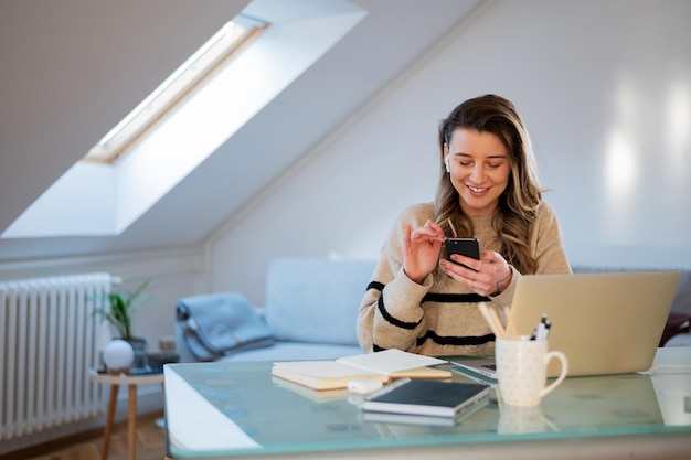 Mujer que usa un teléfono inteligente mientras trabaja en casa y usa una computadora portátil