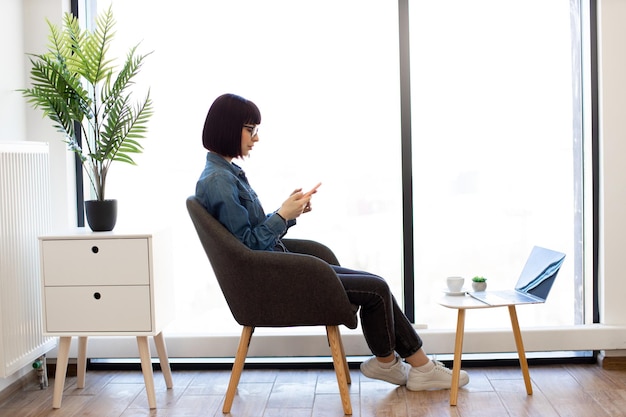 Mujer que usa un teléfono inteligente mientras trabaja en una oficina moderna