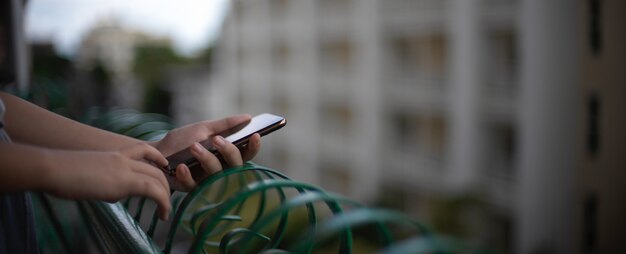 Una mujer que usa el teléfono inteligente para relajarse mientras está de pie en el balcón