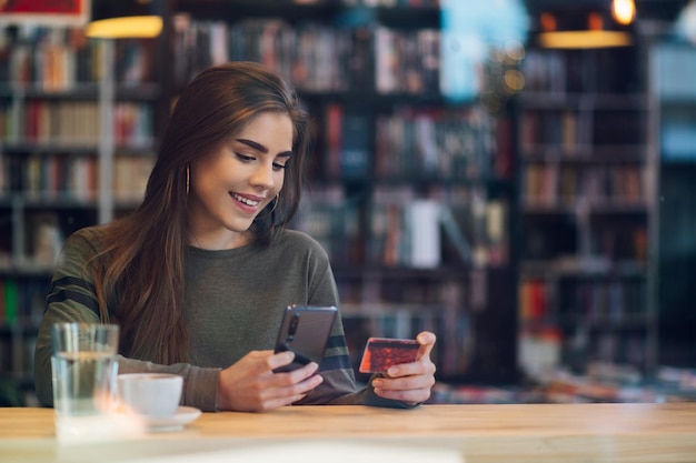 Mujer que usa un teléfono inteligente y una tarjeta de crédito para comprar en línea en un café