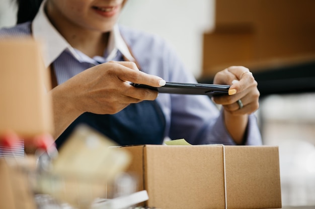 Una mujer que usa un teléfono inteligente para tomar fotografías frente a las cajas de paquetes Cajas de paquetes para empacar productos que entregan productos a través de empresas de mensajería privadas Conceptos de venta y compras en línea