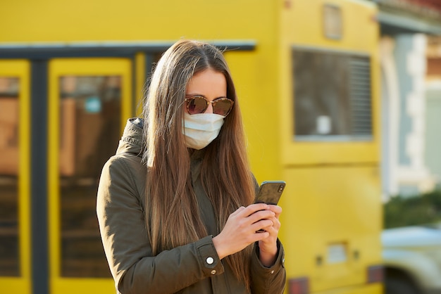 Una mujer que usa un teléfono inteligente usa una mascarilla médica para evitar la propagación del coronavirus en una calle de la ciudad