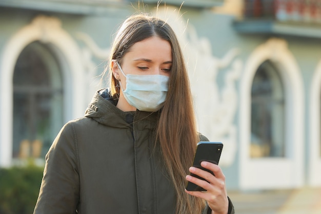 La mujer que usa un teléfono inteligente usa una mascarilla médica para evitar la propagación del coronavirus en una calle