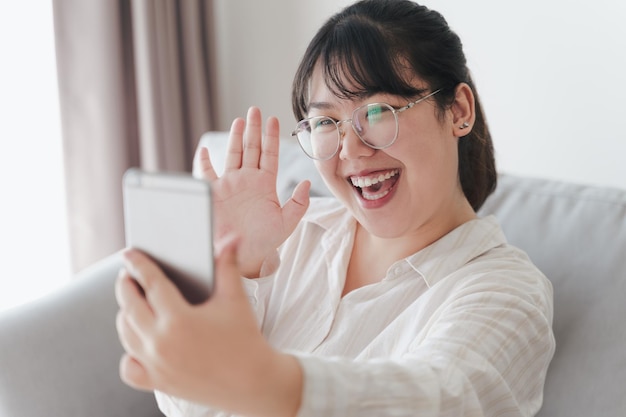 Mujer que usa un teléfono inteligente para una videoconferencia con amigos agitando la mano haciendo un gesto de hola