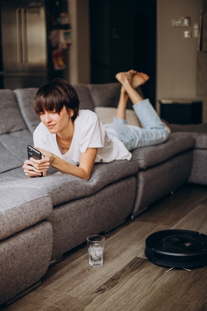 Mujer que usa el teléfono mientras el robot aspirador limpia el piso