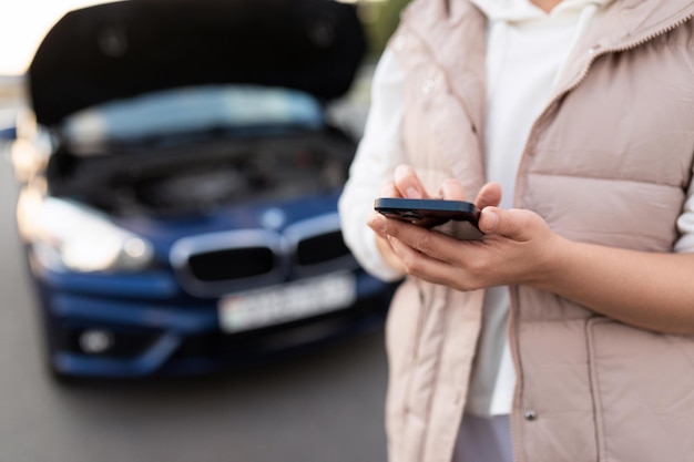 Una mujer que usa un teléfono móvil llama a un servicio de emergencia para evacuar un automóvil al lado de un automóvil abierto