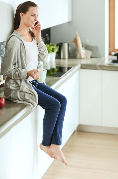 Mujer que usa el teléfono móvil que se sienta en cocina moderna