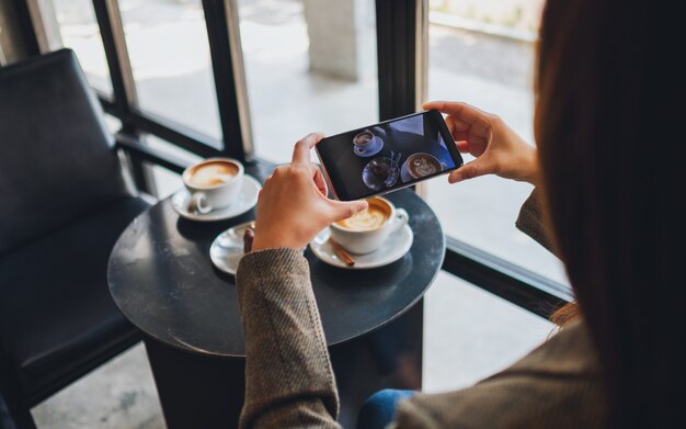 Una mujer que usa el teléfono móvil para tomar una foto de un café y un refrigerio antes de comer en el café