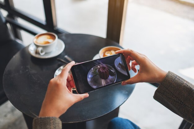 Foto una mujer que usa el teléfono móvil para tomar una foto de un café y un refrigerio antes de comer en el café