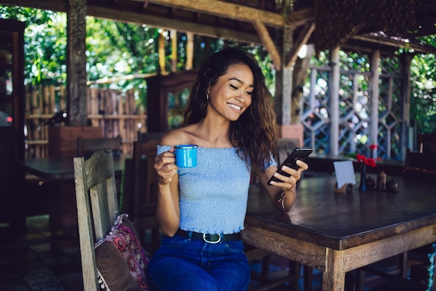 Mujer que usa el teléfono con una taza en la mano sentada al aire libre