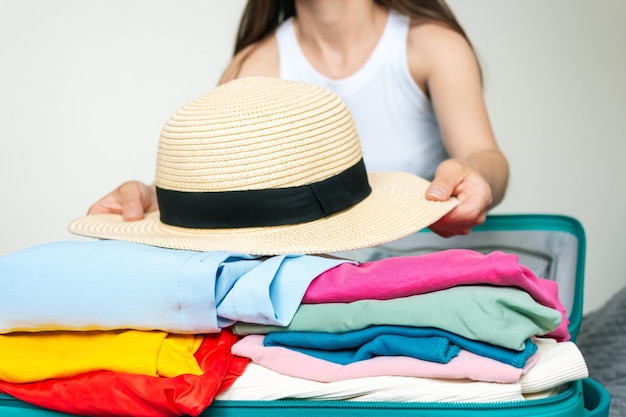 mujer que va de vacaciones al mar en el extranjero poniendo cosas de colores de verano y sombrero de paja en una maleta verde