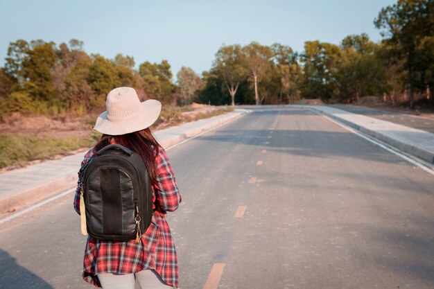 Mujer que viaja con mochila caminando en campo de carretera de asfalto