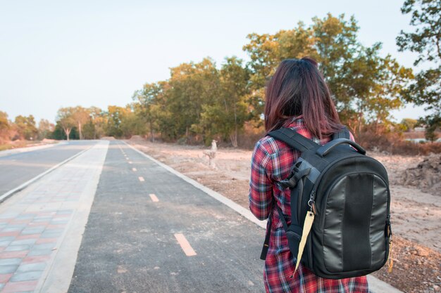 Foto mujer que viaja con mochila caminando en campo de carretera de asfalto