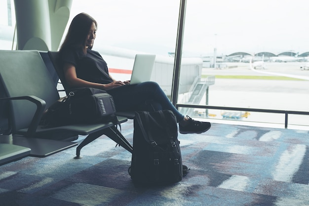 Una mujer que viaja con ordenador portátil mientras está sentado en el aeropuerto