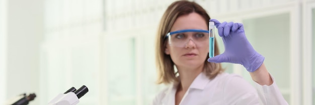 Mujer química mirando el tubo de ensayo con líquido azul frente al microscopio en el laboratorio