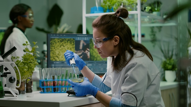 Mujer química tomando ADN líquido del tubo de ensayo con micropipeta en placa de Petri analizando la mutación genética