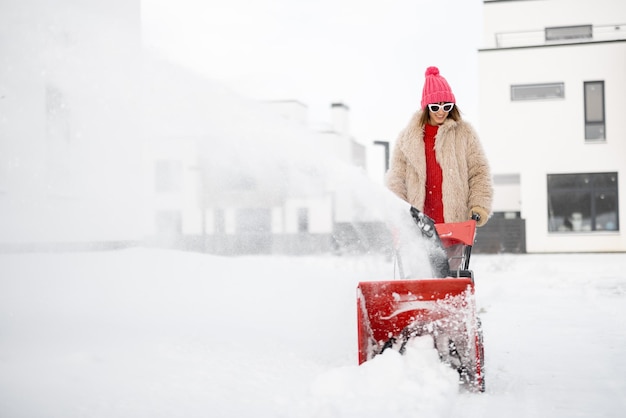 La mujer quita la nieve con una máquina quitanieves cerca de la casa