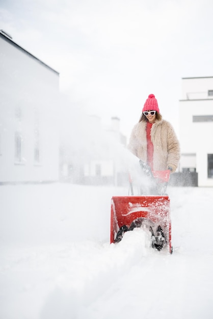 La mujer quita la nieve con una máquina quitanieves cerca de la casa