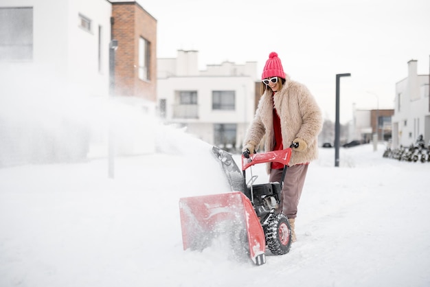 La mujer quita la nieve con una máquina quitanieves cerca de la casa