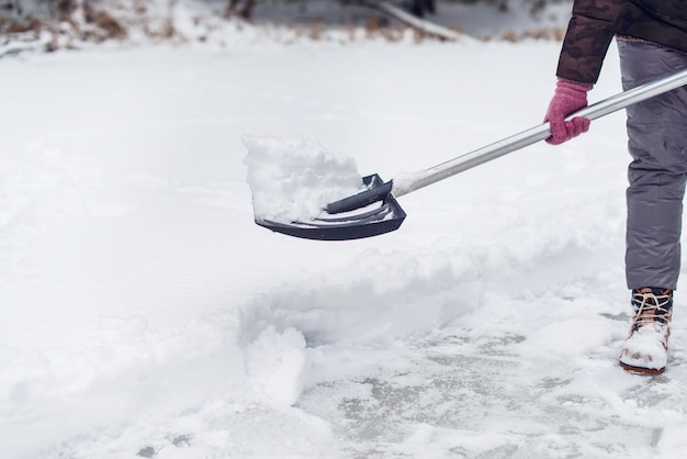 Mujer quitando la nieve con una pala en invierno. Limpieza de pistas de hielo