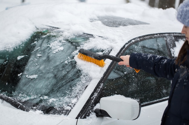 Mujer quitando la nieve del parabrisas del coche