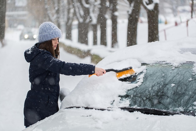 Mujer quitando la nieve del parabrisas del coche