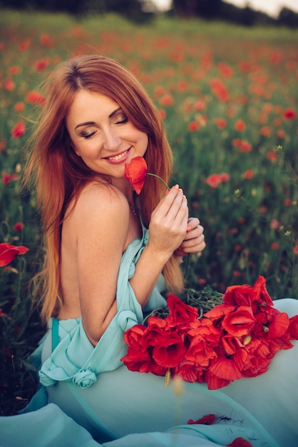 Mujer con ramo de amapolas en sus manos se sienta en campo de amapolas en flor