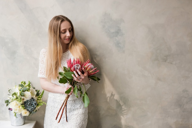 Mujer con ramo de flores protea king sobre fondo de pared. Regalo de niña hermosa, entrega de ramos de flores, concepto de tienda florística