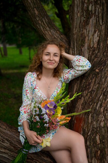 Una mujer con un ramo de flores sentada en un árbol en un parque y sonriendo