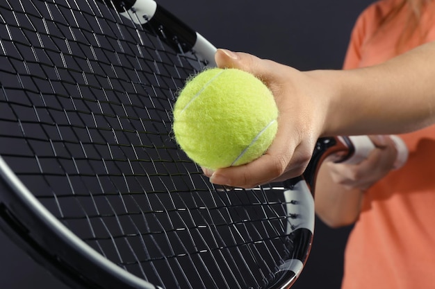 Mujer con raqueta de tenis y pelota sobre fondo gris oscuro