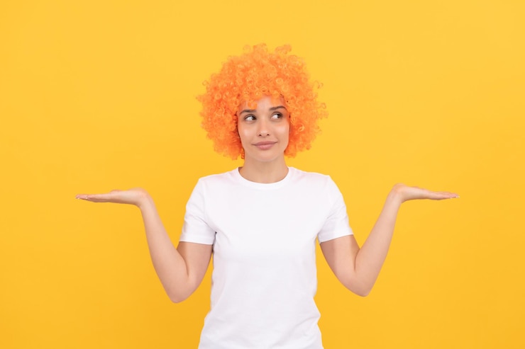 Foto mujer rara con peluca de payaso que presenta el producto expresa emociones positivas chica divertida con peluca naranja día de los inocentes tiene que elegir el concepto de elección espacio de copia aspecto de fiesta elegante