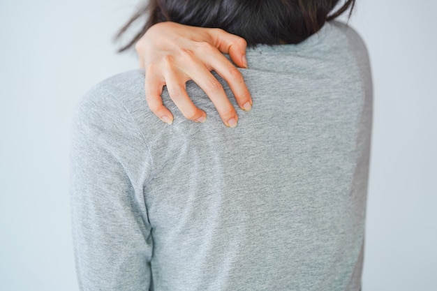 Una mujer rascándose la espalda a través de su camisa. Concepto de enfermedad de la piel.