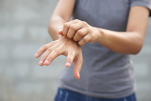 Mujer rascarse el brazo por picazón sobre fondo gris claro Las causas de la picazón en la piel incluyen picaduras de insectos