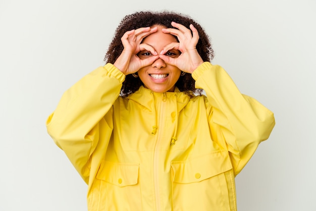 Mujer de raza mixta afroamericana joven aislada emocionada manteniendo el gesto ok en el ojo.