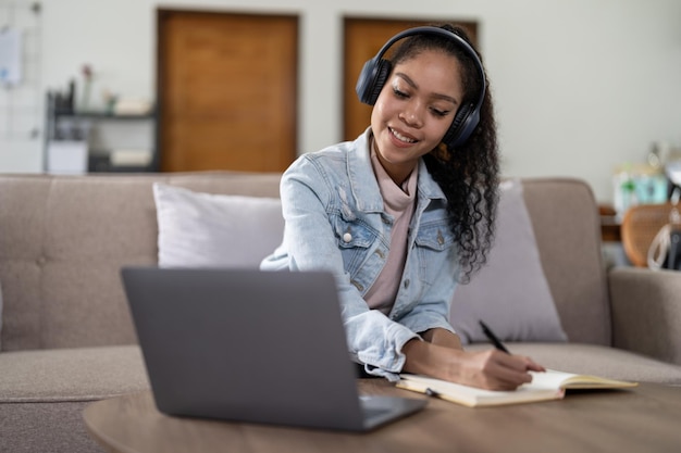 Mujer de raza mixta con auriculares viendo seminario web escribir notas estudiar en línea con profesor en línea estudiante africana aprendiendo idioma curso de computación en computadora portátil escuchar traducir conferencia