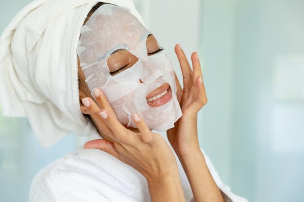 Foto mujer de raza mixta con bata de baño y mascarilla limpiadora en el baño